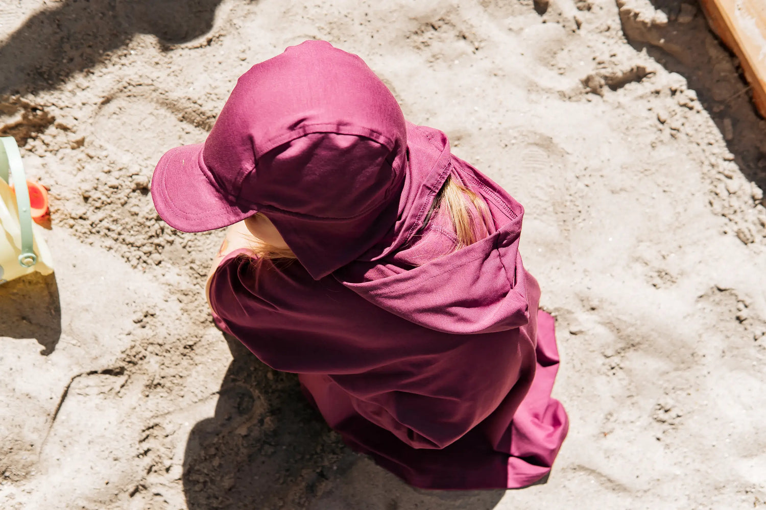 Kind trägt einen weichen UV-Schutzponcho mit Kapuze im Garten an einem sonnigen Sommertag. Der leichte Kinderponcho mit UPF 50+ schützt empfindliche Haut ganz ohne chemische Beschichtung.