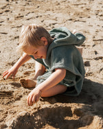 Weicher Kinder-Strandponcho Dino aus saugfähigem Baumwoll-Frottee mit Kapuze, Dinozacken und Bauchtasche – ideal für Bad, Pool oder Urlaub am Meer.