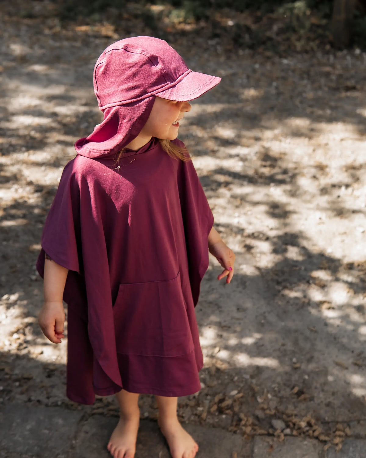 Kind trägt Set aus Überzieh Poncho und Sonnenhut mit Lichtschutzfaktor 50+ nach dem Schwimmen im Urlaub