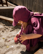 Kind mit UV Poncho und Sonnenhut mit Lichtschutzfaktor 50+ beim Spielen im Kindergarten Sandkasten 