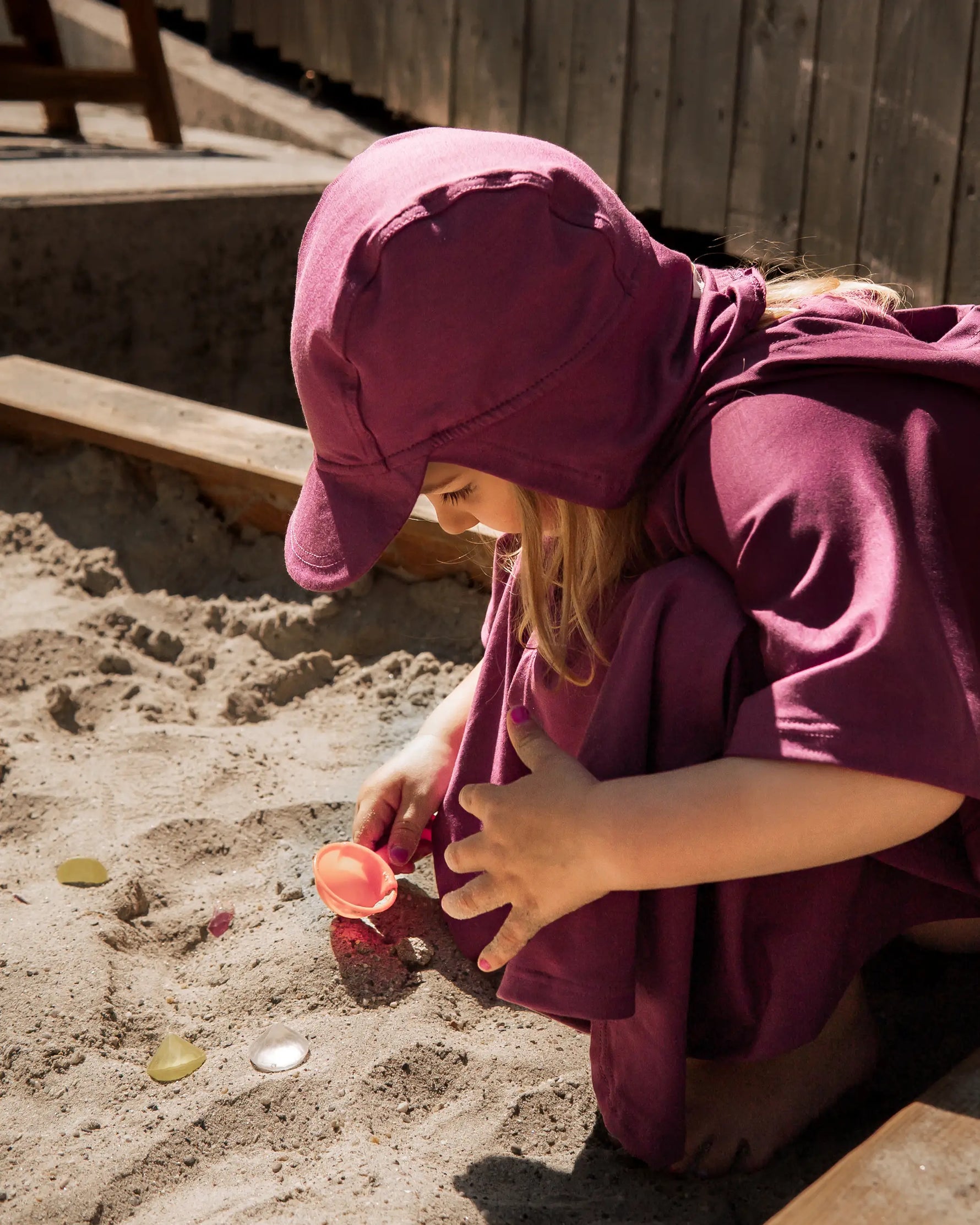 Kind mit UV Poncho und Sonnenhut mit Lichtschutzfaktor 50+ beim Spielen im Kindergarten Sandkasten 